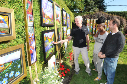 L’artiste peintre Yves-Groulx montrant ses toiles à deux visiteurs dans son atelier-jardin.